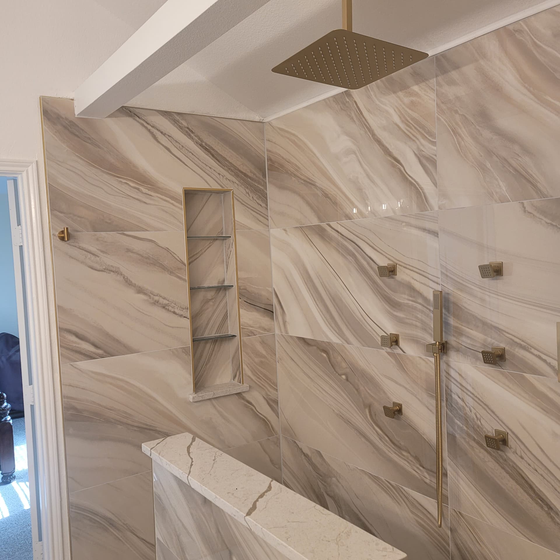 Custom shower with marble-look slabs, gold fixtures, niche and body sprays