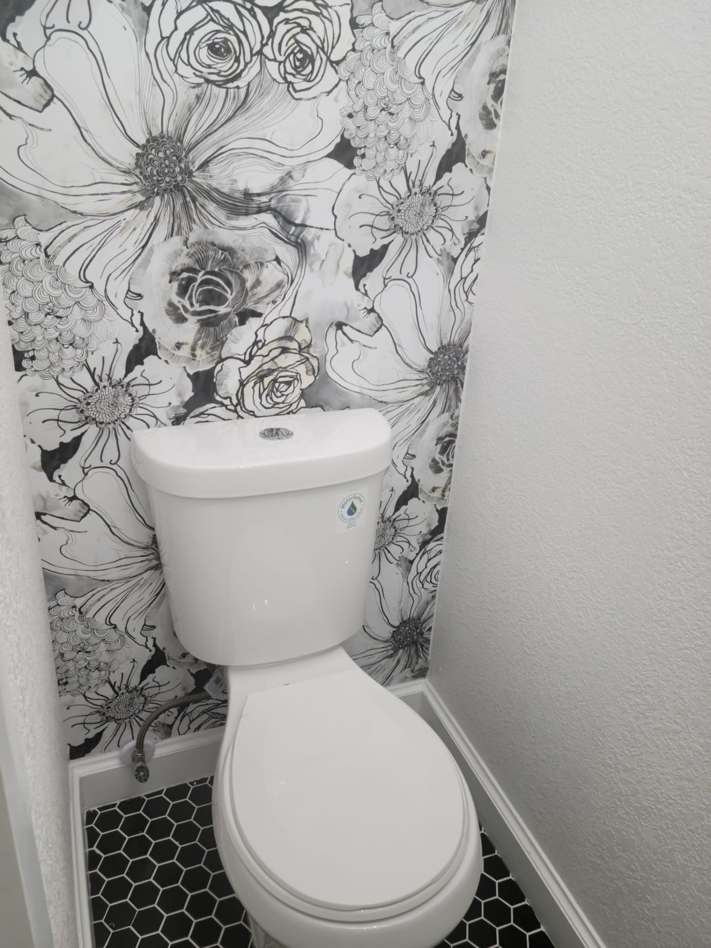 Water closet with bold floral wallpaper and black hexagon floor tile